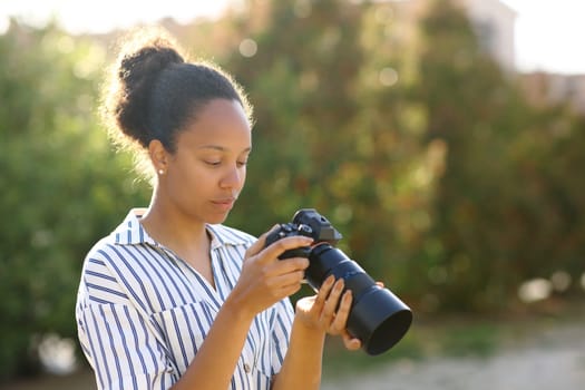 Concentrated black photographer checking result on mirrorless camera in a park