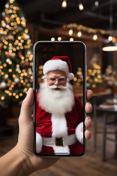 Hand holding smartphone with video chat with Santa Claus on blurred Christmas background