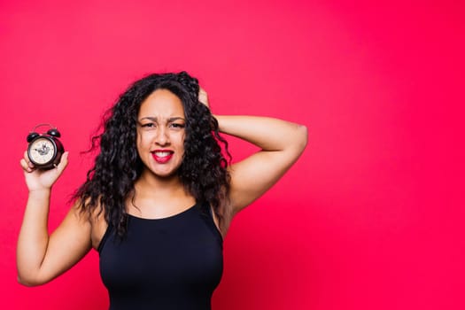 Smiling young african american woman posing isolated on a red background with clock