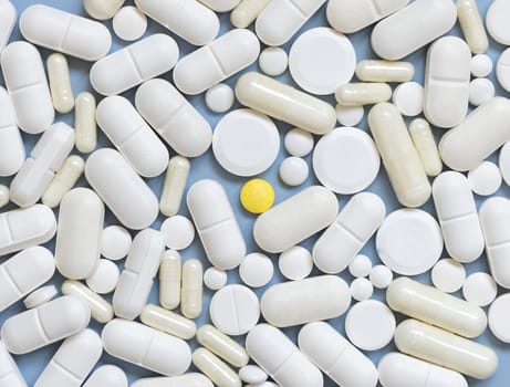 Mix of white medical capsules and pills with one yellow pill in the middle on light blue top view. Medicinal treatment. Taking dietary supplements and vitamins. Assorted pharmaceutical products