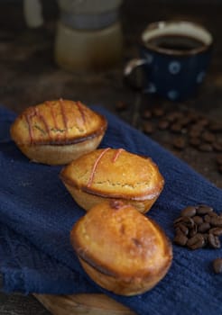 Pasticciotto leccese pastry filled with egg custard cream on dark blue napkin. Whole pasticiotties served for typical apulian breakfast with coffee, close up. Table decorated with coffee beans