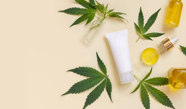 Pipette with CBD oil and cream tube near green cannabis leaves on beige top view, copy space. Organic skincare beauty products, natural alternative cosmetics