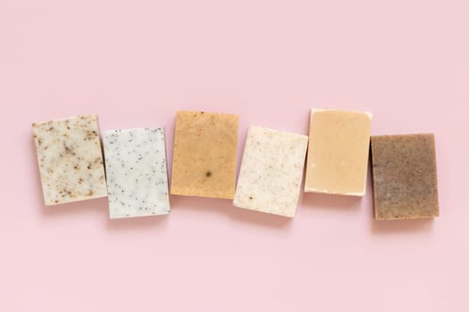 Beige and brown handmade soap bars in a line on light pink top view, copy space. Natural herbal products for Spa and skin care. Using organic handmade skincare products in everyday routine