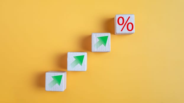 Wooden block with percentage symbol and up arrow on yellow background. Interest rate and dividend concept,  return on stocks and mutual funds, long term investment for retirement.