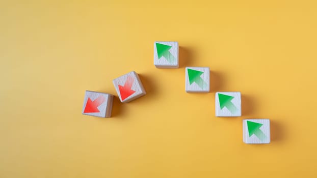 Green arrow and red arrow on wooden block represents economy trending downwards on yellow background. Economy recession crisis, inflation, stagflation, business and financial loss concept.