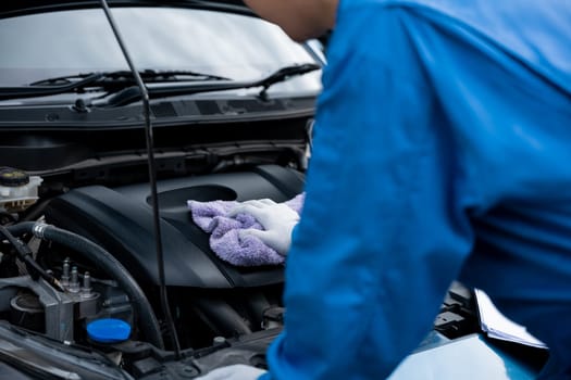 Close-up shot of an Asian mechanic's hand in a blue shirt writing on a paper, in an auto repair shop.