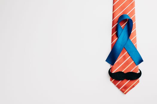A blue ribbon adorned with a mustache and necktie, symbolizing Prostate Cancer Awareness, signifies support for those affected by the illness. Men's healthcare and World Cancer Day concept.