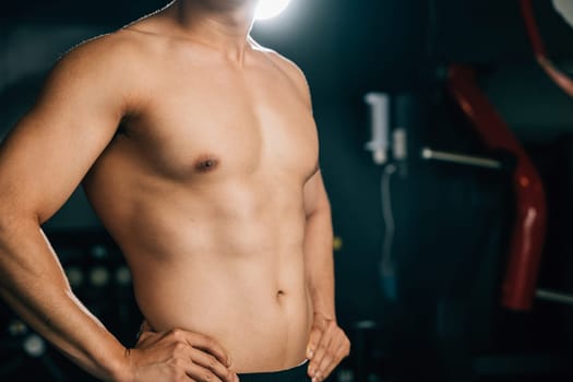 A smiling athletic Asian man, with a toned body and strong bicep muscles, stands on his waist in a gym, while his trainer helps him with his training. Healthy fitness Lifestyle with copy space