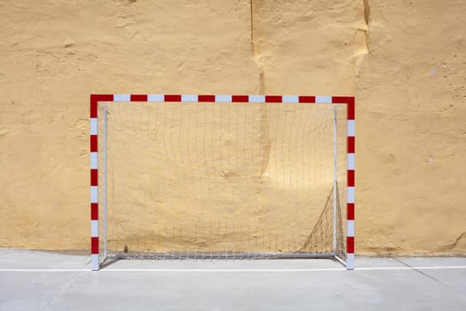 Soccer ball and goal with net against plastered wall background. Football at school yard scenery