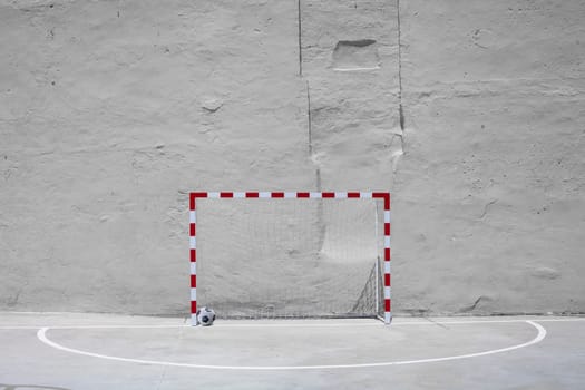 Soccer ball and goal with net against plastered wall background. Football at school yard scenery