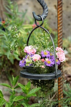 Bouquet of small roses and asters hanging in a glass vase in the garden.