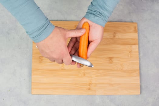 Peel carrots with scraper sharpener, prepare healthy food with vegetables, fresh organic nutrition, cooking ingredients