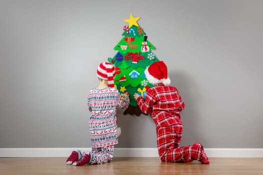 Children decorating wall of the room by green toy fir Christmas tree. Concept of the Xmas and New Year.