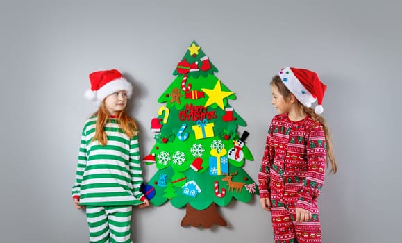 Two little girls decorating wall of the room by green toy fir Christmas tree. Concept of the Xmas and New Year.