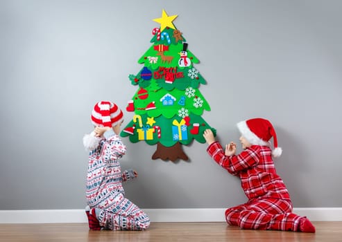 Children decorating wall of the room by green toy fir Christmas tree. Concept of the Xmas and New Year.