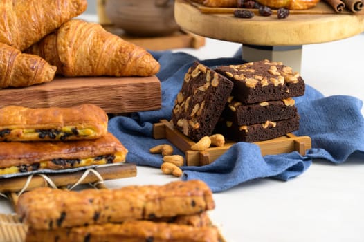 Chocolate brownies with cashew nut on wooden board and blue fabric, croissant and danish with raisins. Fresh bakery bread for breakfast