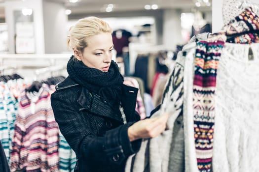 Woman shopping clothes. Shopper looking at clothing indoors in store. Beautiful blonde caucasian female model.