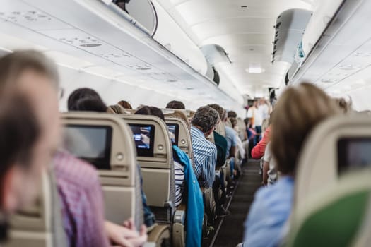 Interior of modern commercial airplane with passengers on their seats waiting to taik off.