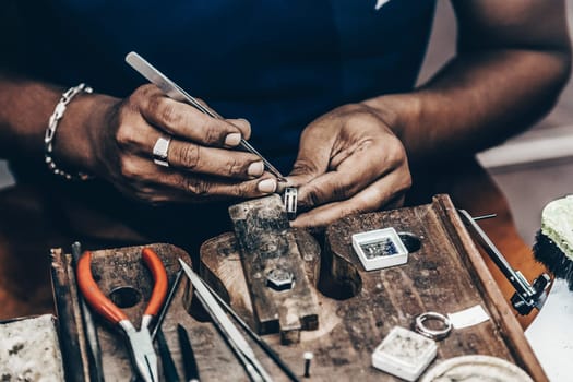 Jeweler making handmade jewelry on vintage workbench. Craft of jewelery making. Repairing ring by inlaid tight gem.