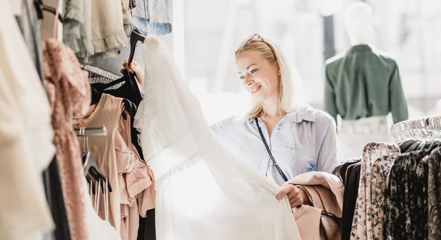 Woman shopping clothes. Female shopper looking at fashionable clothes indoors in clothing store.