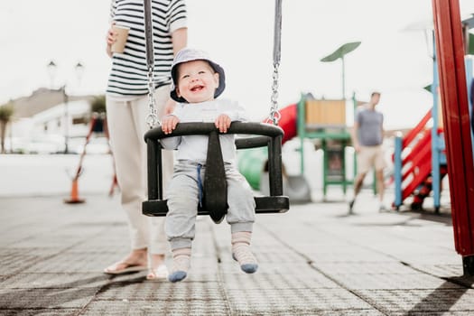 Mother pushing her infant baby boy child on a swing on playground outdoors