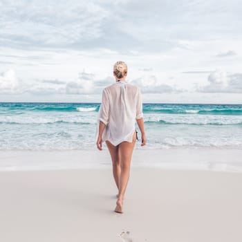 Woman wearing white loose tunic over bikini on Mahe Island, Seychelles. Summer vacations on picture perfect tropical beach concept.