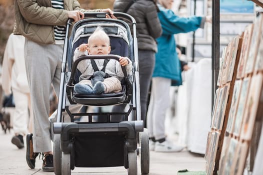 Mother walking and pushing his infant baby boy child in stroller in crowd of people wisiting sunday flea market in Malaga, Spain