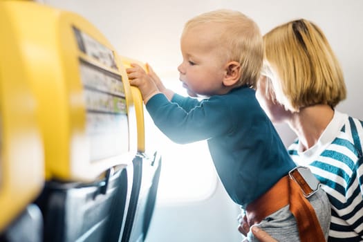 Mom and child flying by plane. Mother holding and playing with her infant baby boy child in her lap during economy comercial flight. Concept photo of air travel with baby. Real people