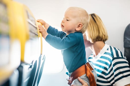 Mom and child flying by plane. Mother holding and playing with her infant baby boy child in her lap during economy comercial flight. Concept photo of air travel with baby. Real people
