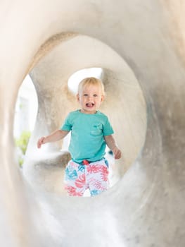 Child playing on outdoor playground. Toddler plays on school or kindergarten yard. Active kid on stone sculpured slide. Healthy summer activity for children. Little boy climbing outdoors