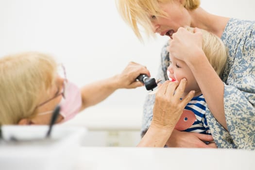 Infant baby boy child being examined by his pediatrician doctor during a standard medical checkup in presence and comfort of his mother. National public health and childs care care koncept