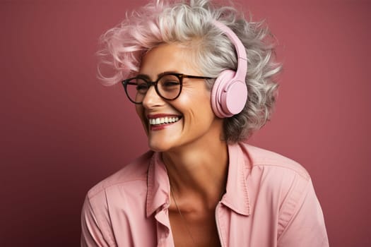 beautiful and cheerful gray-haired woman in glasses, pink clothes and headphones, on a color background