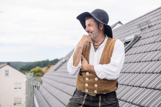 Roofer in traditional gear standing on roof of residential home looking proud