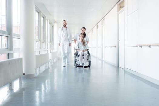 Doctor, nurse, and patient in wheelchair walking on hospital corridor
