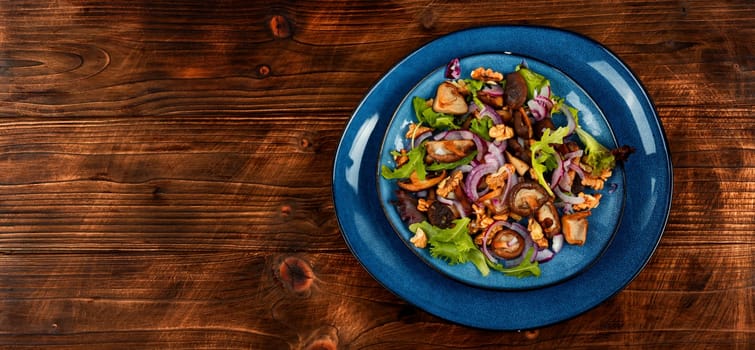 Warm salad with roasted mushrooms, herbs and walnuts on black wooden table. Healthy vegetarian food. Top view, copy space, rustic style.