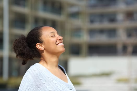 Happy black woman breathing fresh air standing in the street