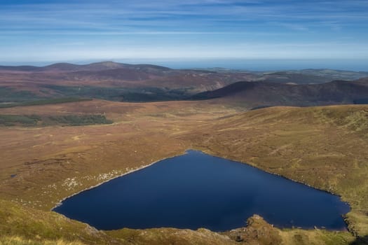 View from the top of Tonelagee mountain on heart shaped lake, Lough Ouler, reflecting blue sky. Hiking in Wicklow Mountains, Ireland