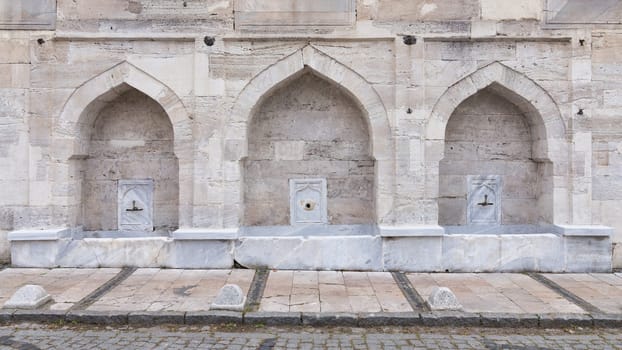 External stone wall of 16th century historic Atik Valide Mosque with row of ablution fountains, located in Uskudar, Istanbul, Turkey, built by Nurbanu Sultan, the mother of Sultan Selim II