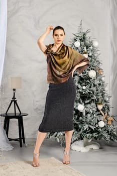 Young woman in tight black dress with glitter and silk scarf posing near the Christmas tree