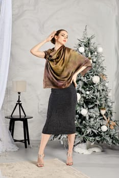 Fashionable young woman in tight dress and silk shawl posing near the Christmas tree