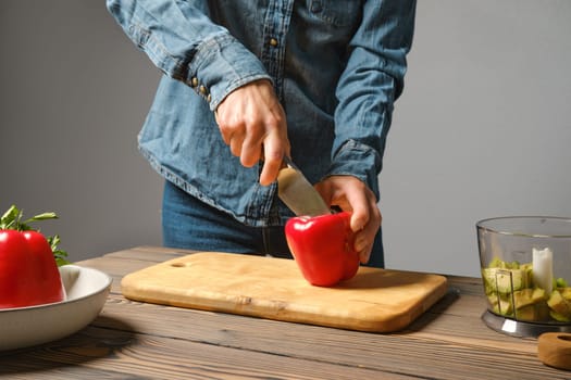 Unrecognizable woman cutting bell pepper on half in the kitchen
