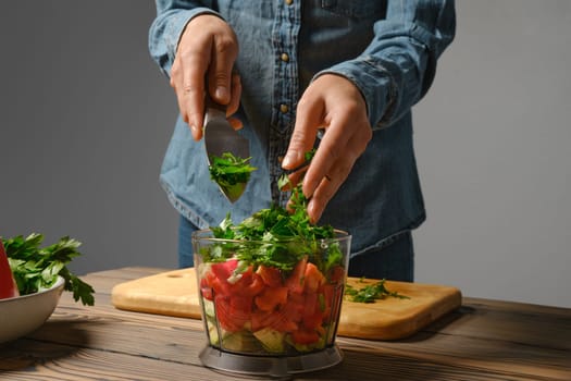 Close up view of female hands dropping chopped parsley into blender in the kitchen