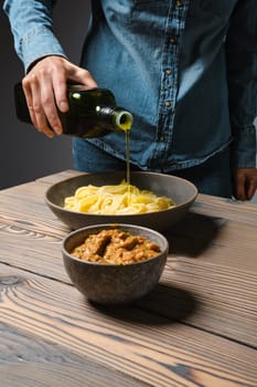 Unrecognizable woman pouring olive oil into plate with pasta fettuccine