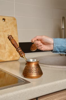 Hand of unrecognizable woman pours ground coffee into a turk
