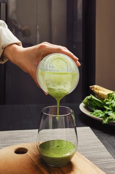 Hand pouring healthy smoothie in glass in the kitchen