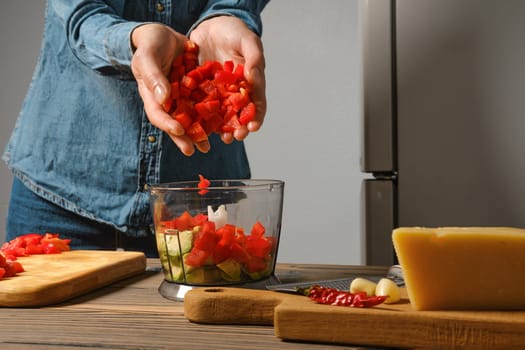 Close up view of female hands dropping chopped red bell pepper into blender in the kitchen