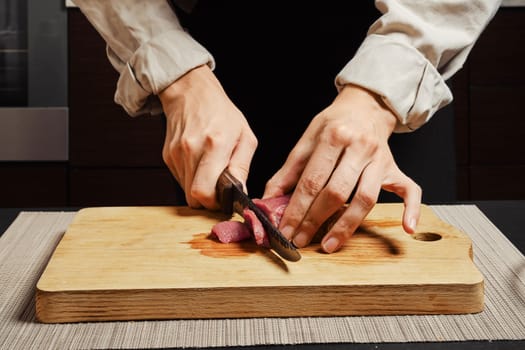 Unrecognizable woman slicing raw beef fillet on cutting board
