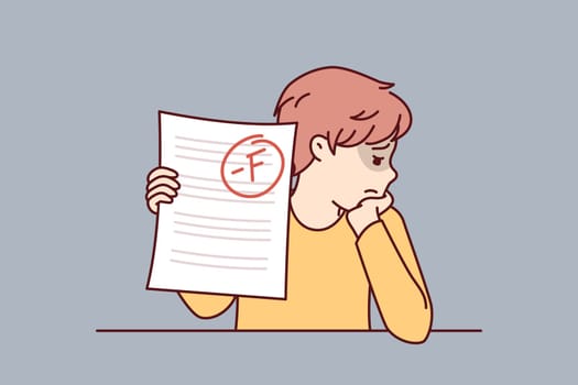 Schoolboy is sad because of poor test score and educational failures caused by lack of motivation to study at school. Boy is upset after receiving exam in primary school and needs help of tutor
