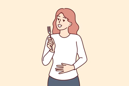 Hungry woman with fork in hands touches stomach, demonstrating good appetite and desire to dine. Hungry girl needs food and looks at screen with smile, waiting for waiter with order
