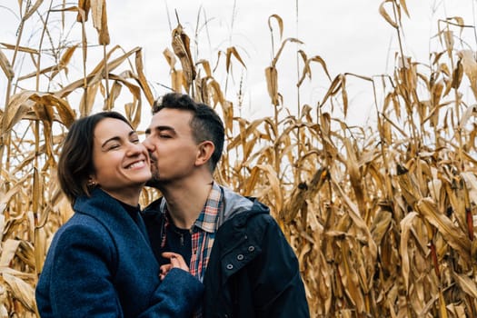 A man kisses a happy woman on the cheek while walking outside the city in a cornfield in autumn.